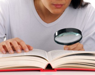 Mujer leyendo un libro sujetando una lupa.