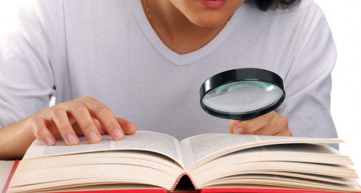Mujer leyendo un libro sujetando una lupa.