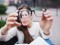 Closeup portrait of young women with glasses. She has eyesight problems and is squinting his eyes a little bit. Beautiful girl is holding eyeglasses right in front of camera with two hand